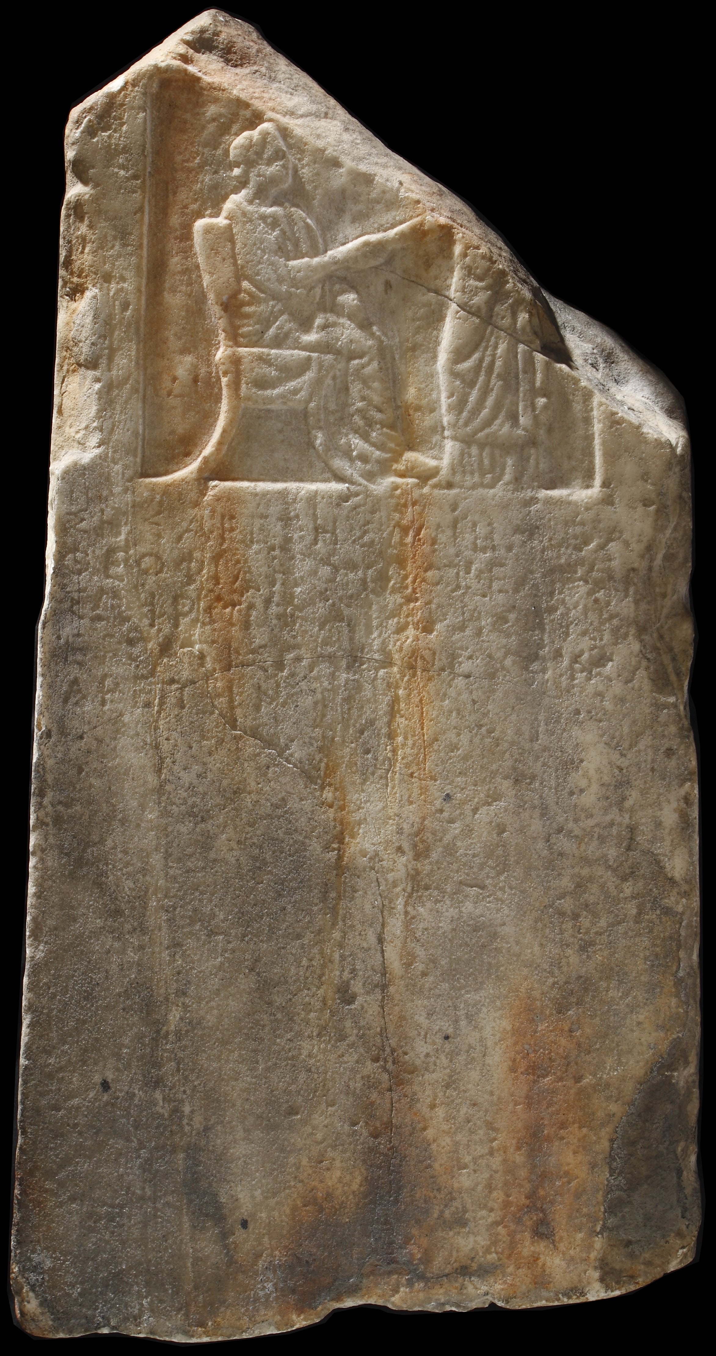 A marble funerary stele: at the top, a seated female figure, on the left, shakes hands with a standing figure.Below, a four line inscription.
